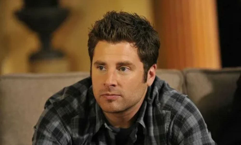 A professional photo of actor James Roday Rodriguez smiling. He is dressed in a suit, looking at the camera, standing against a plain background.